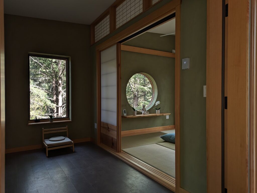 A photo of two rooms in the new Abbot's Kuti. One has only a chair under a rectangular window. The other has a live edge wood altar in front of a round window. The floor is olive color tatami mats.